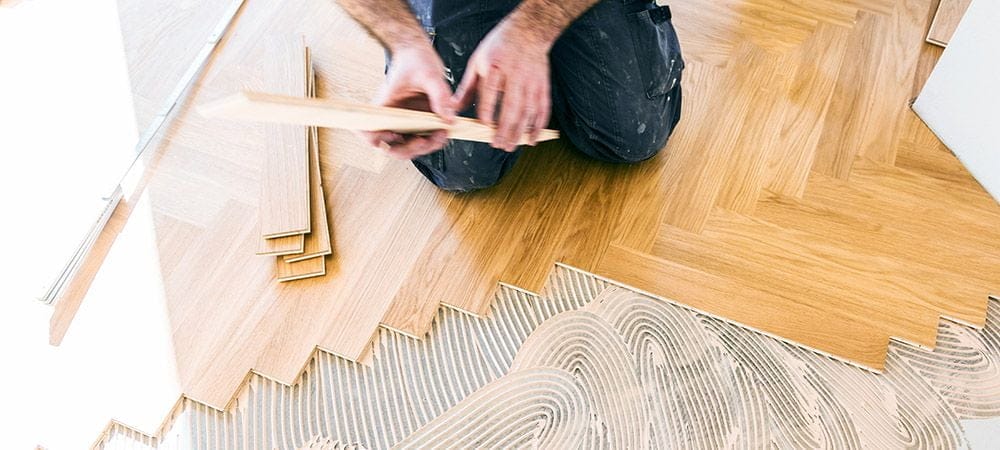 Mand lægger trægulv i sildebensmønster