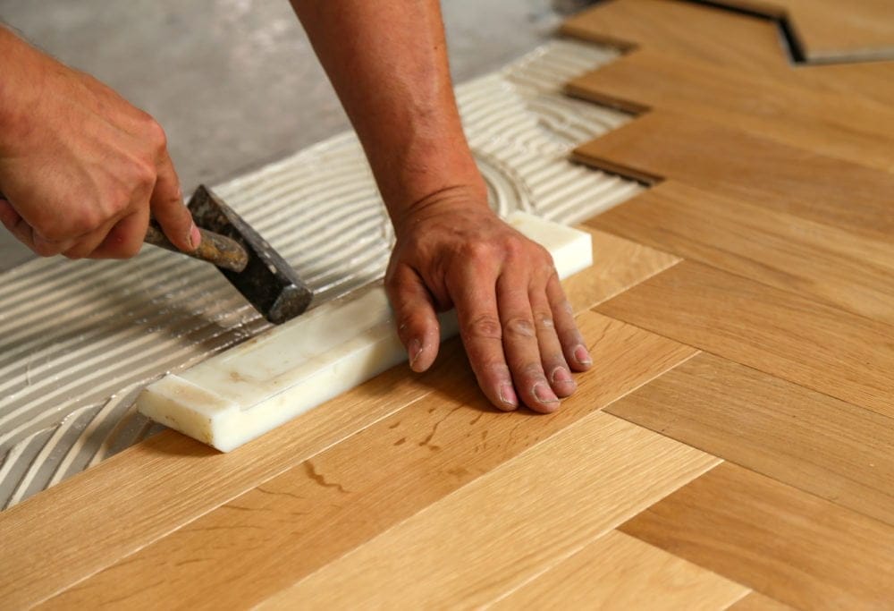Person installerer sildebensparketgulv med hammer