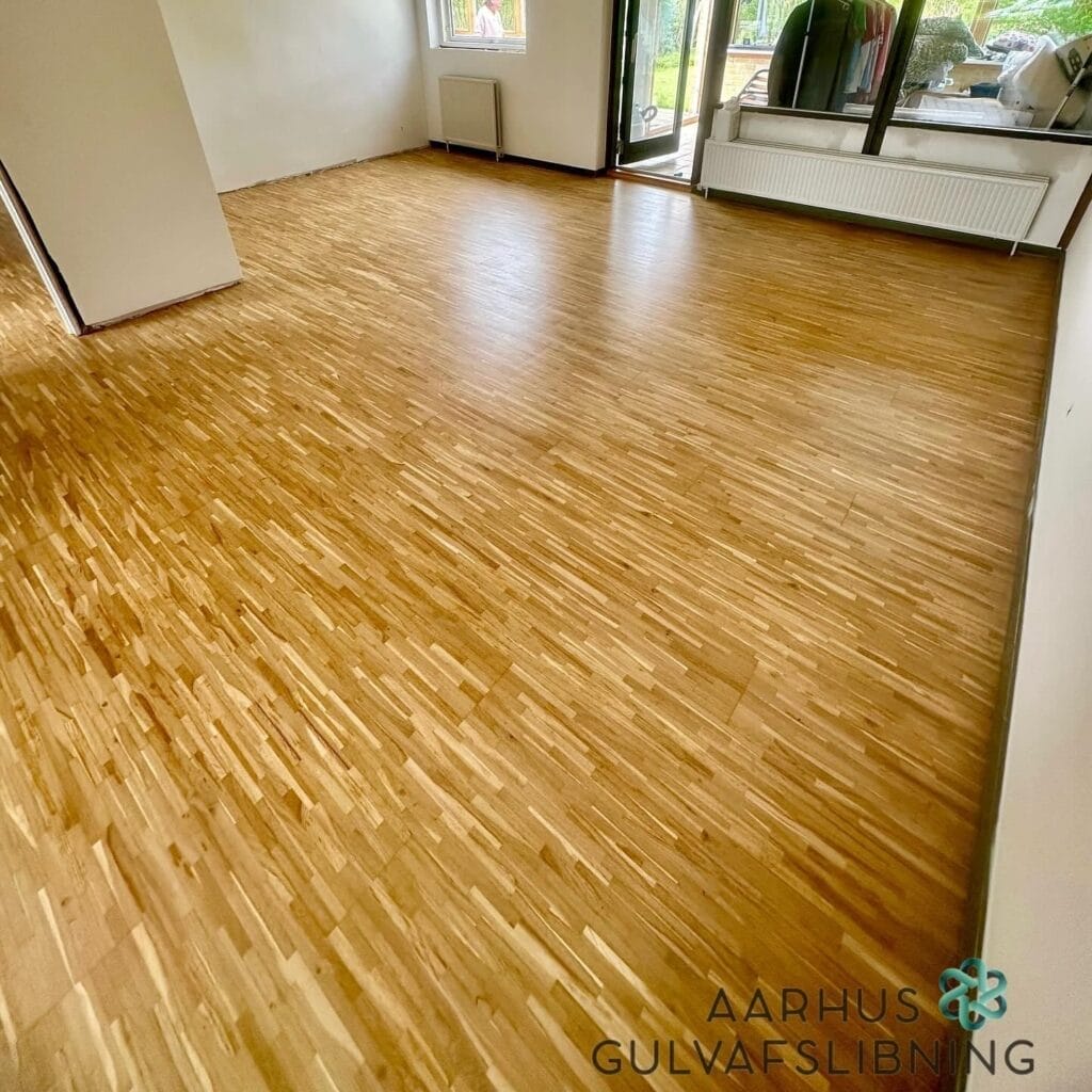 Nyrenoveret trægulv i lys stue med store vinduer.