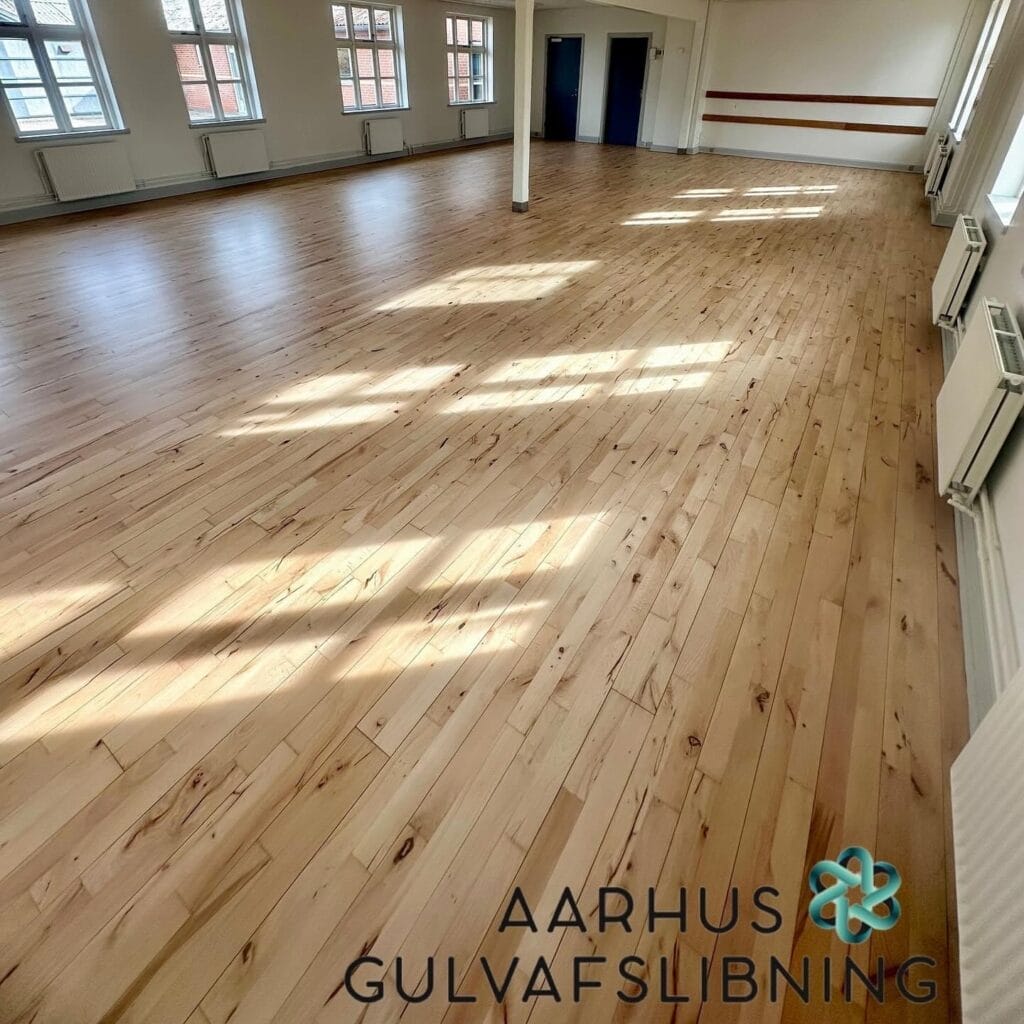 Nyafslebet lyst trægulv i stort rum med vinduer